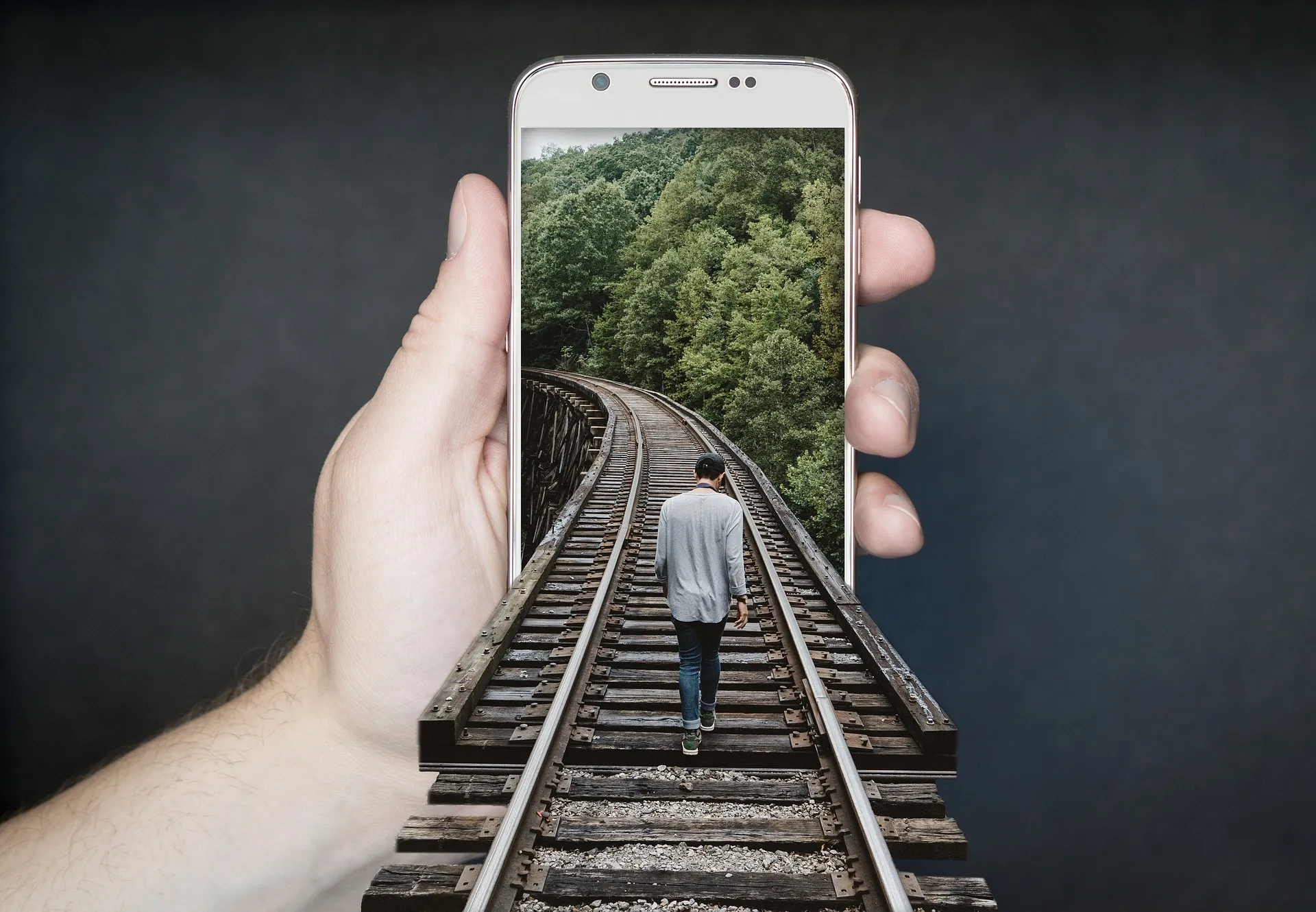 A hand holding a smartphone with a train track emerging from the screen